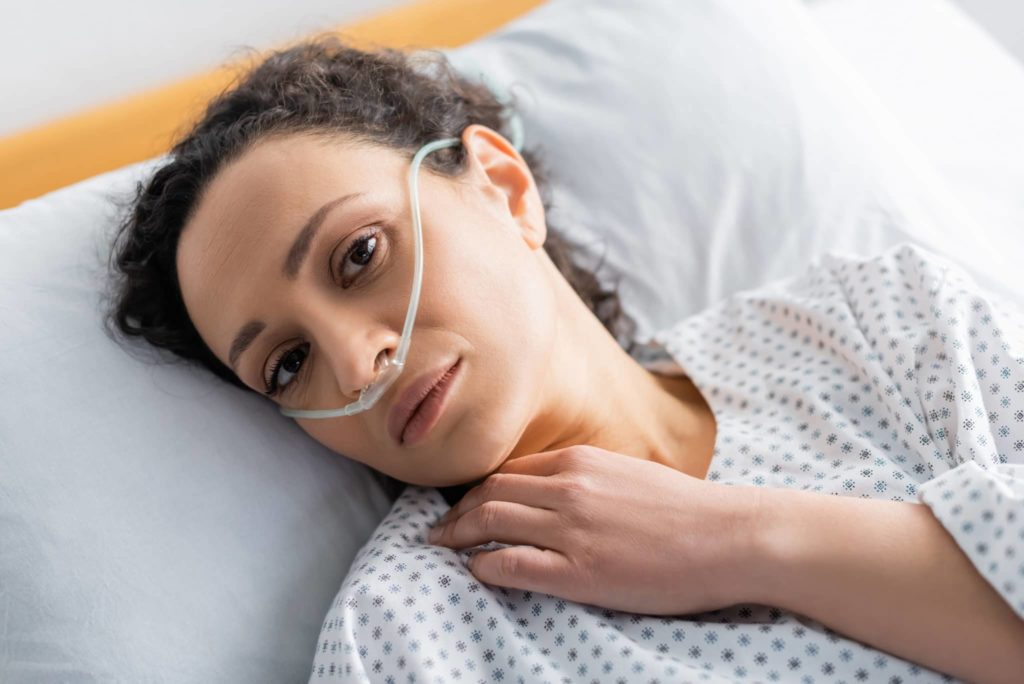 overhead view of sick african american woman with nasal cannula looking at camera while lying in hospital bed